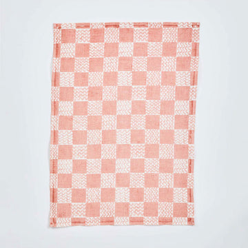 A pink and white checkered tea towel featuring squiggly lines in the white boxes is laying against a white background.