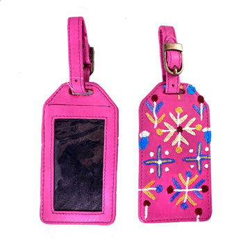 Front and back view of a luggage tag in pink with a clear sleeve on the back and embroidered with artwork by Rosie Ross on the front.
