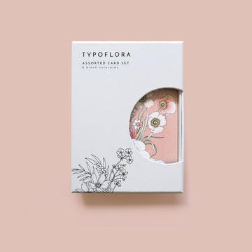 A white box set of card with a cut out showing the cards inside illustrated with flowers.