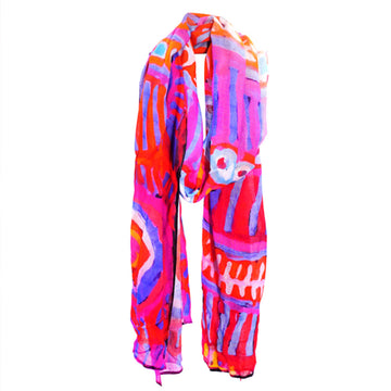 A cotton scarf is laid like it was wrapped around a neck. The scarf features artwork by Murdie Nampijinpa Morris in pinks and blues.