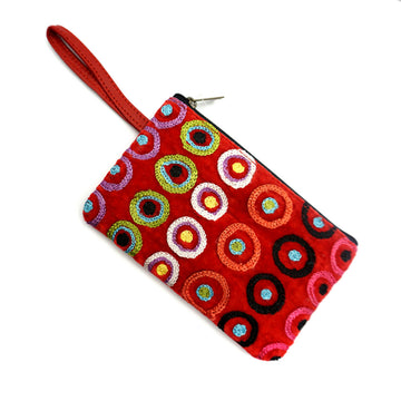 A red velvet coin purse with a wrist strap and embroidered with artwork by Daisybell Kulyuru on the front.