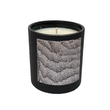 A wax candle inside a black container with artwork on the front by Damien Coulthard. 