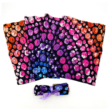 A baby swaddle is fanned out and printed with artwork by Olivia Wilson. There is another one rolled up in front.