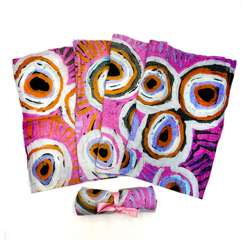 A baby swaddle is fanned out and printed with artwork by Murdie Nampijinpa Morris. There is another one rolled up in front.