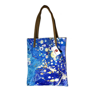 A blue tote bag featuring artwork by Stephen Jupurrurla Nelson with brown straps.