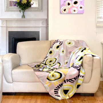 A cotton throw printed with artwork by Murdie Morris is laying on a couch in front of a fireplace.