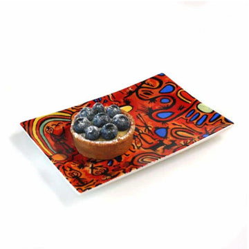 A small rectangle plate pictured printed with artwork by Cedric Varcoe and with a tart on top.