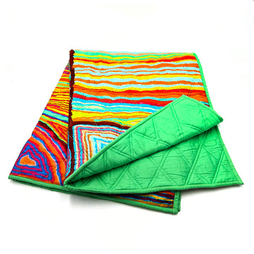 A folded up quilted baby blanket printed with artwork by Judy Watson on the top and green on the bottom.