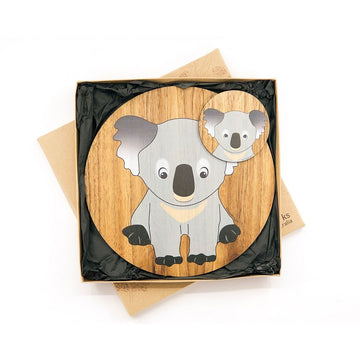 A matching set of a wooden round coaster and table mat printed with an illustration of a koala in a box.