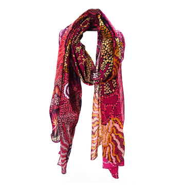 A cotton scarf is laid like it was wrapped around a neck. The scarf features artwork by Damien and Yilpi Marks in red and yellow.