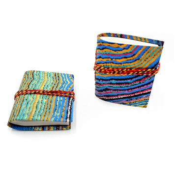 Two small journals pictured, one is lying down and the other is standing up.  The covers of both are printed with artwork by Liddy Walker with red string around them.