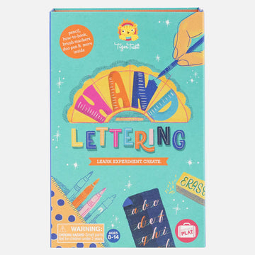 Front cover of an activity set titled 'Hand Lettering Learn Experiment Create' with an illustration of a hand colouring in with a blue pen and an illustration of markers inside a pencil case and hand drawn letters.