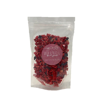 A clear bag filled with freeze dried davidson plum chips and a pink round sticker on the front with the text 'Warndu Feel Good Davidson Plum'.