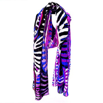 A cotton scarf is laid like it was wrapped around a neck. The scarf features artwork by Murdie Nampijina Morris in purple, blue and black.