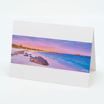 A white landscape card featuring a panoramic photograph of Pinky beach with rocks on the beach and a sunset sky.