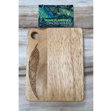 A wooden cutting board with a leaf etched on the left side. The brand name's card can be seen at the top with the name 'Ngarga Warendj' written in green.