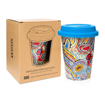 A reusable coffee cup printed with artwork by Judy Watson and a blue lid is pictured on the right. Behind it on the left is the brown packaging box with a cut out of the cup on the front showing the cup inside.