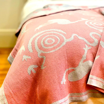 A grey and pink baby blanket is draped over the edge of a bed.