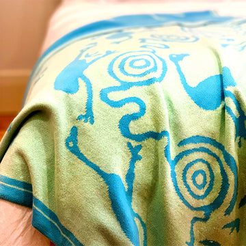 A green and blue baby blanket is draped over the edge of a bed.