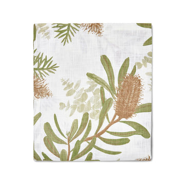 A folded up white tablecloth printed with banksia flowers and leaves.