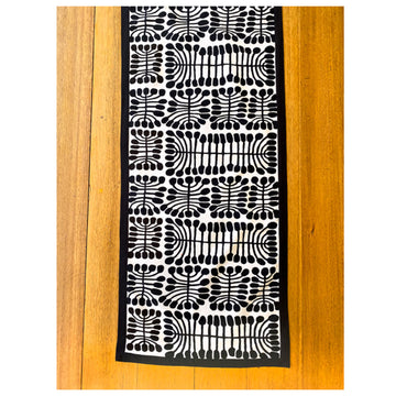 Top down view of a wooden table with a table runner on top. The runner is black and white and features artwork by Mitjili Napurrula.