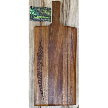 A long rectangle wooden board with a paddle handle and etched with a leaf on the left side.