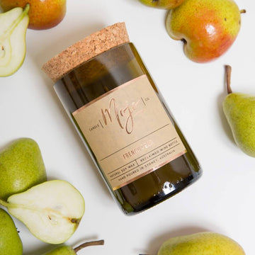 A candle made from a wine bottle with a cork lid lying down surrounded by cut in half pears.