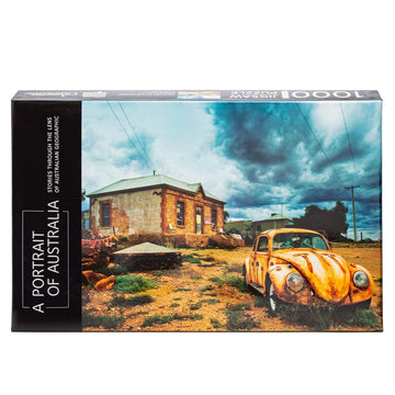 Jigsaw box featuring a photo of a car on land in front of a house with grass patches. The box is standing up.