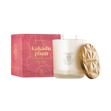Pink box with "Kakadu Plum" in gold writing sitting behind a cream candle with black text, and resting on the right hand side of the candle is a gold embossed lid.