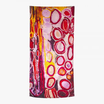 A silk scarf is laid out featuring artwork by Jakayu Biljabu in pinks, reds and yellow.
