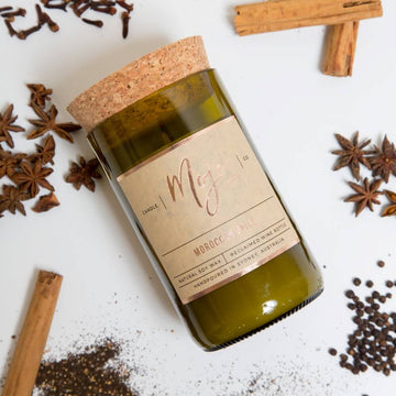 A candle made from a wine bottle with a cork lid. The candle is lying down surrounded by spices.