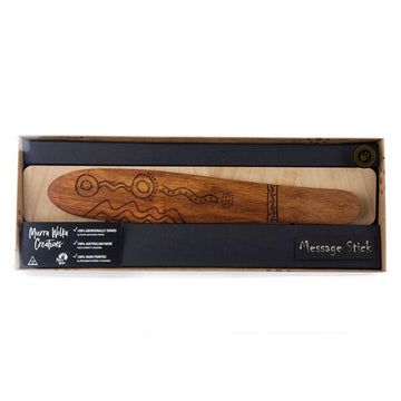 A wooden message stick with carvings is packaged in a box with a plastic lid.