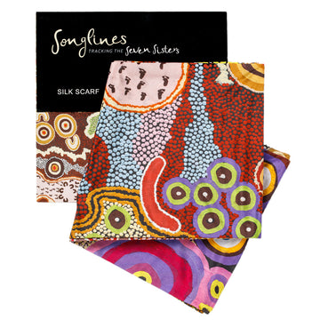 Songlines silk scarf featuring artwork in multicolour in the shape of circles and dots. Behind the scarf is the cardboard packaging slip.