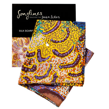 Printed silk scarf with the design 'Minyipuru' with yellow and purple prominent. The packaging slip is behind the scarf.