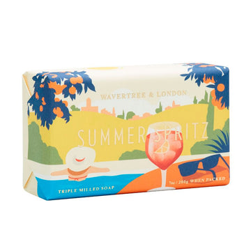 Slightly side on view of a packaged soap coloured in blues, yellows and orange with a wine glass, sunglasses and the back view of a person featured on the front.