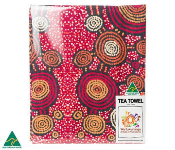 Cotton tea towel, 45cm x 75cm, features artwork by Warlukurlangu artist Teddy Gibson. Red background: red, orange, and black circles joined together by lines; white, orange dot art. Australian made.